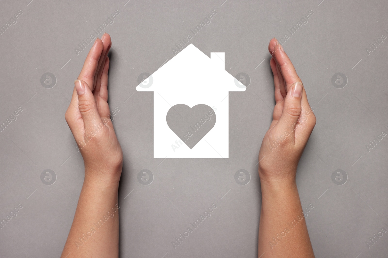 Image of Woman holding hands around paper silhouette of house on grey background, top view. Insurance concept