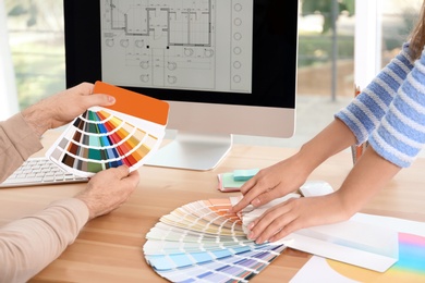 Photo of Designers with paint color palette samples at table, closeup
