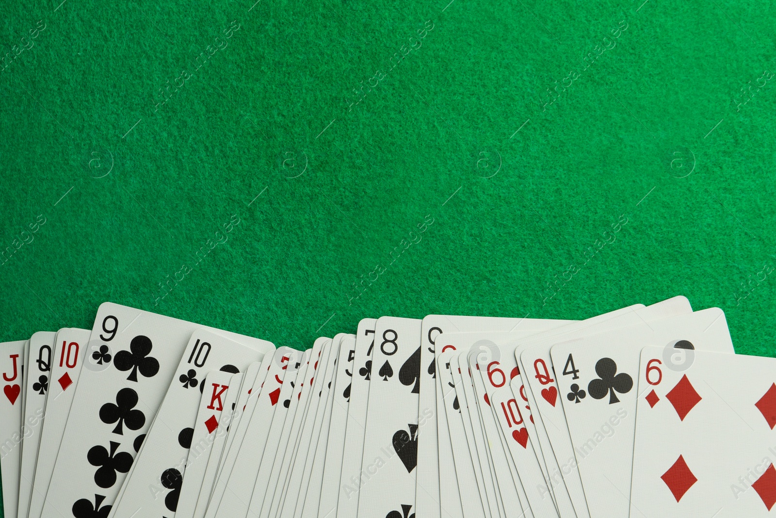 Photo of Deck of playing cards on green table, top view. Space for text