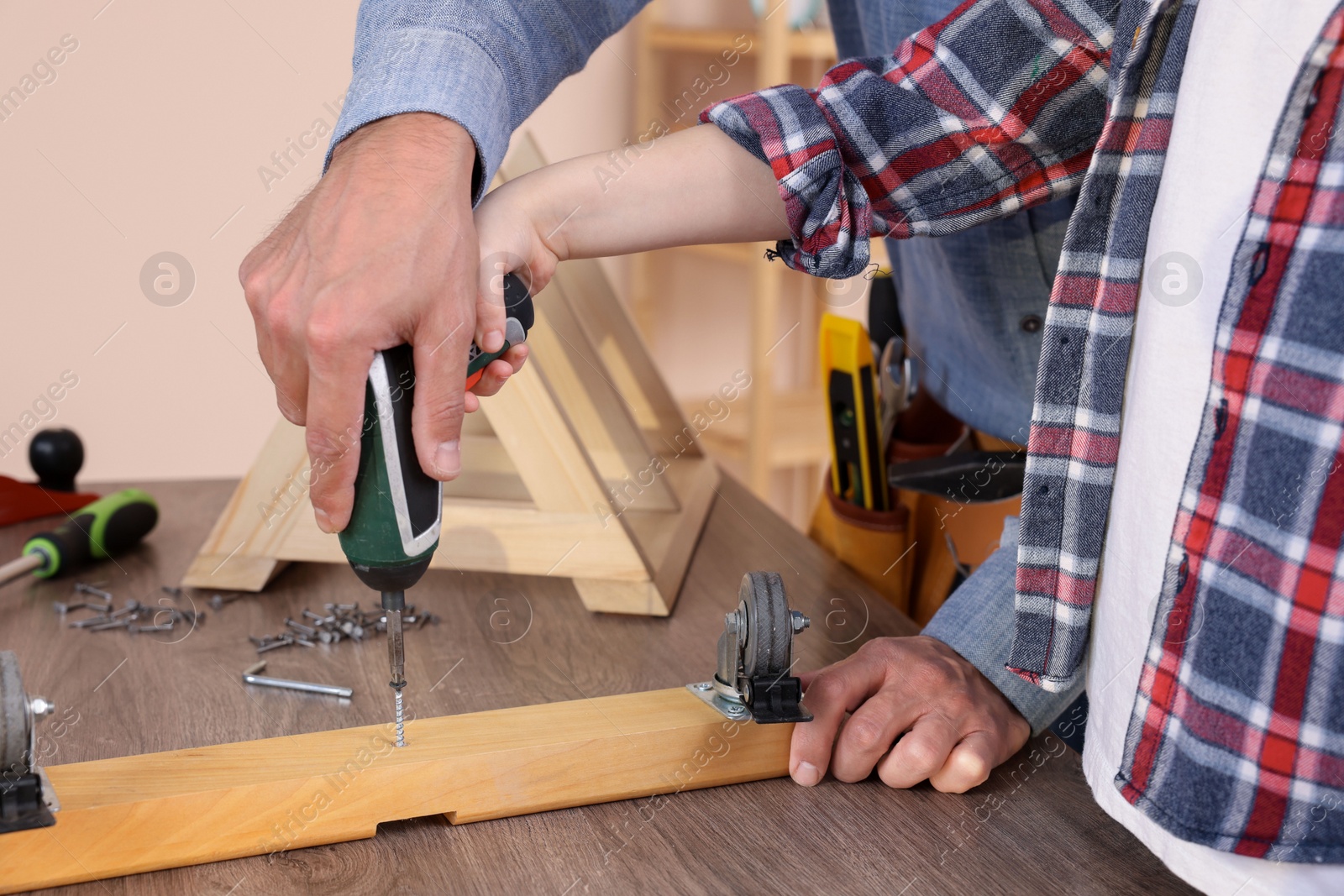 Photo of Father and son screwing wooden plank indoors, closeup. Repair work