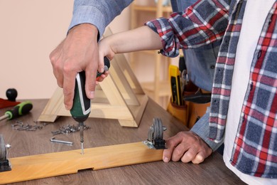 Photo of Father and son screwing wooden plank indoors, closeup. Repair work