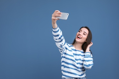 Photo of Attractive young woman taking selfie with phone on color background