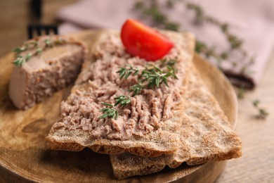 Photo of Crispy crackers with delicious meat pate and thyme served on wooden board, closeup