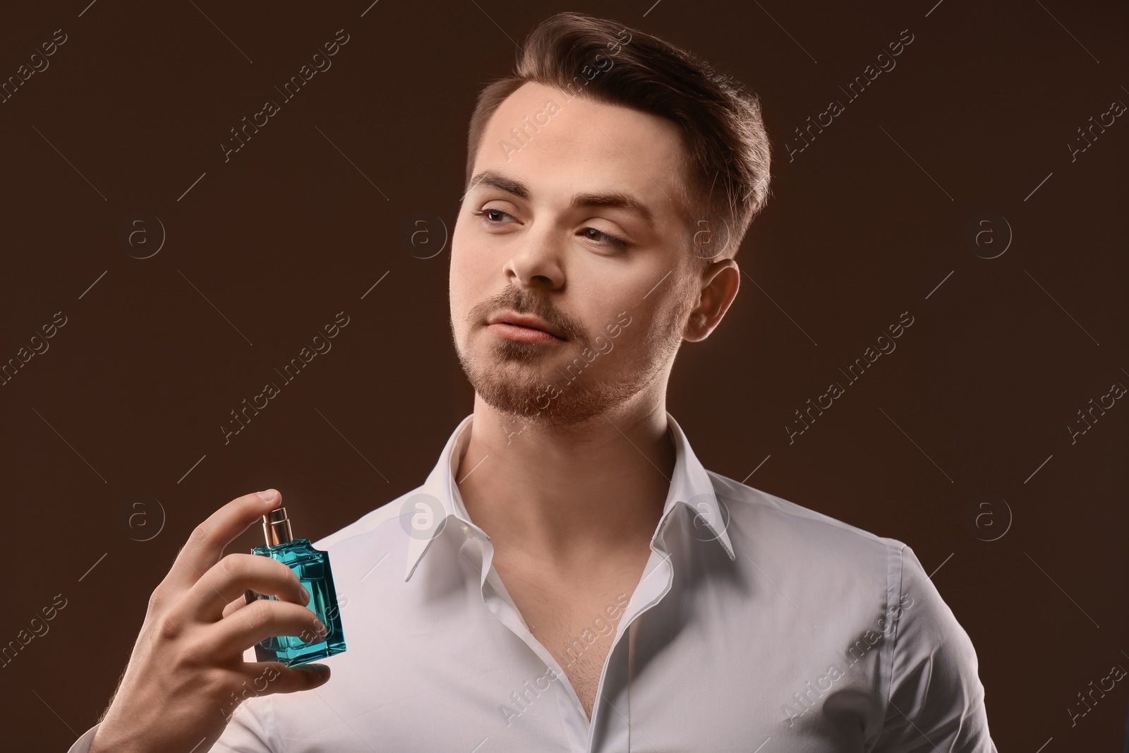 Photo of Handsome man in shirt using perfume on dark background