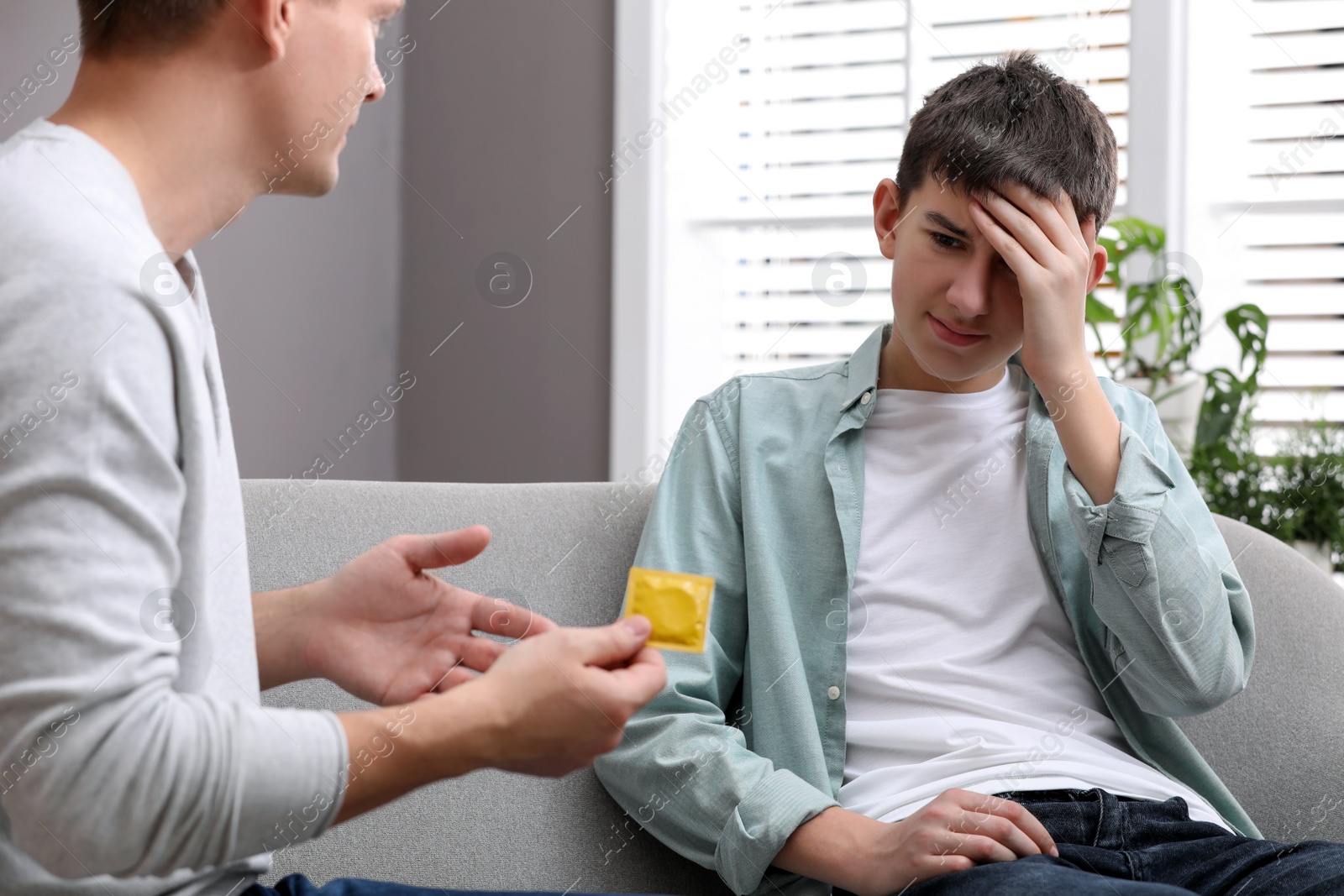 Photo of Father talking with his teenage son about contraception at home. Sex education concept