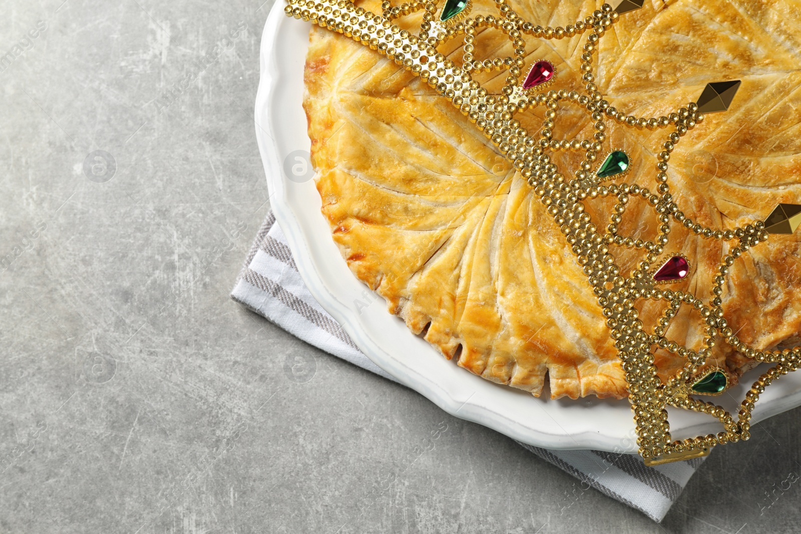 Photo of Traditional galette des Rois with decorative crown on light grey table, flat lay. Space for text