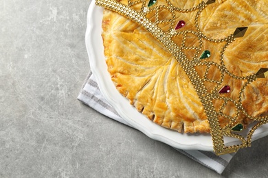 Traditional galette des Rois with decorative crown on light grey table, flat lay. Space for text