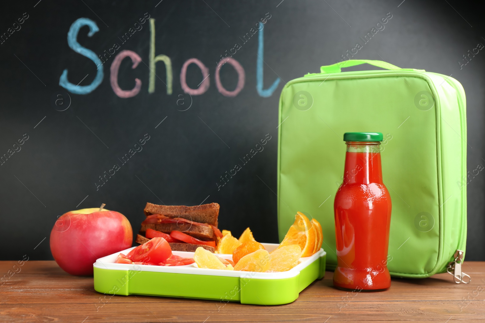 Photo of Appetizing food in lunch box and bag on table near chalkboard with word SCHOOL