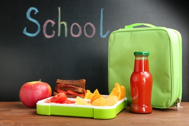 Appetizing food in lunch box and bag on table near chalkboard with word SCHOOL