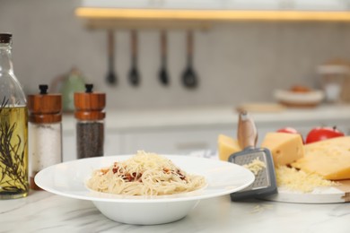 Photo of Delicious pasta with grated cheese and other products on white marble table in kitchen