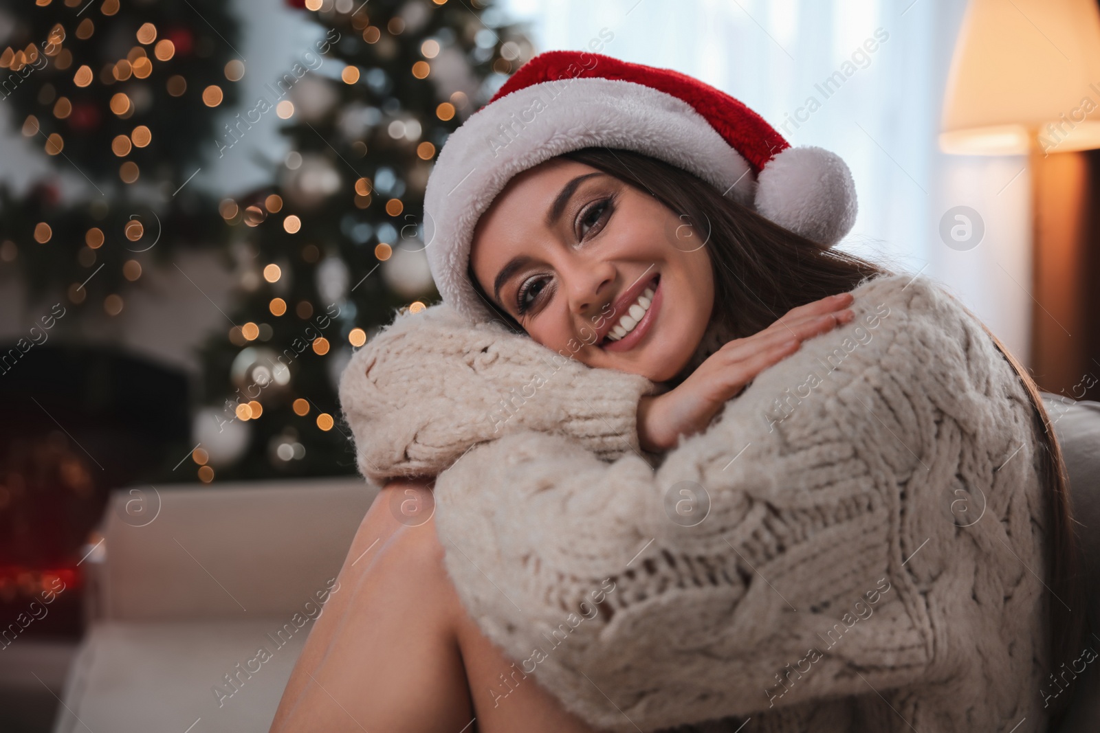 Photo of Beautiful young woman wearing Santa hat in room decorated for Christmas