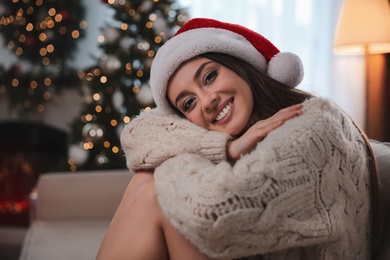 Beautiful young woman wearing Santa hat in room decorated for Christmas