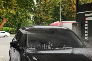 Man washing auto with high pressure water jet at car wash, closeup