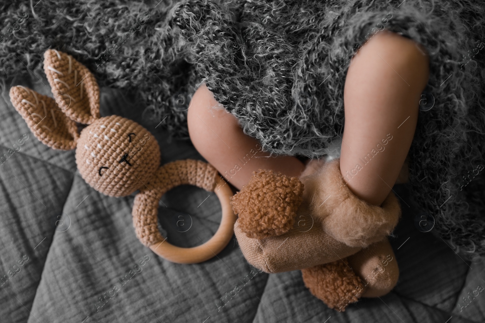 Photo of Adorable newborn baby with grey fluffy blanket and teething toy in bed, closeup