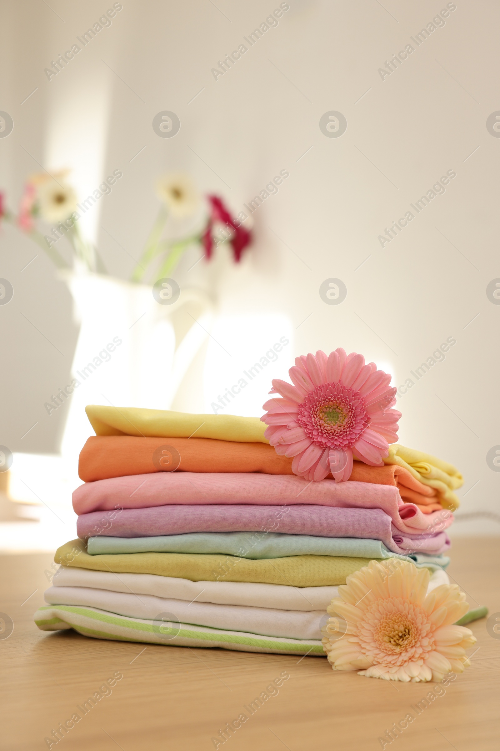 Photo of Stack of clean clothes and flowers on wooden table