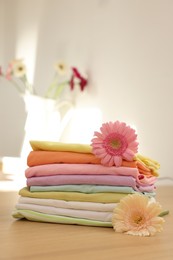 Stack of clean clothes and flowers on wooden table