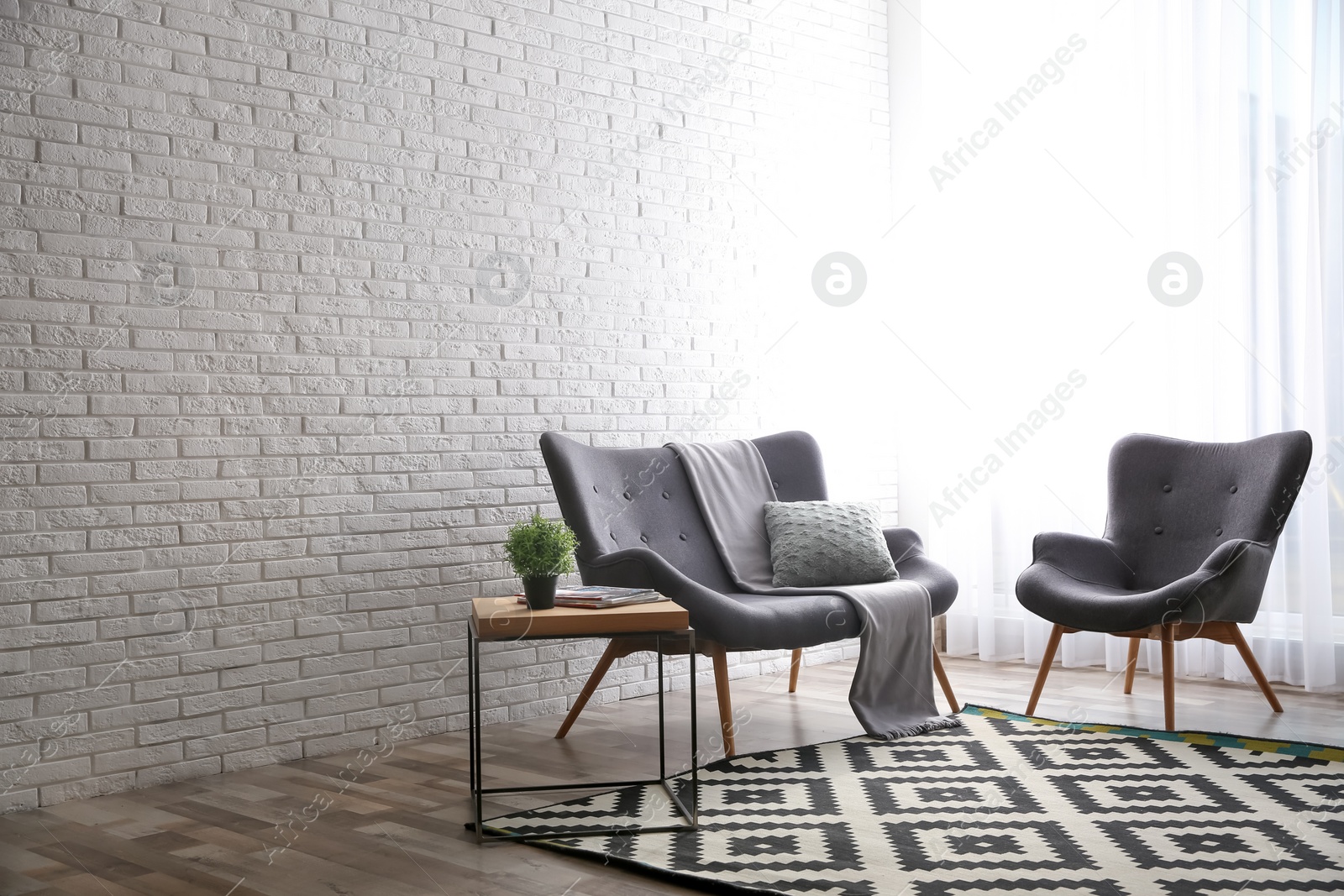 Photo of Stylish sofa and armchair near brick wall in modern living room interior. Space for text