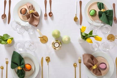 Photo of Festive Easter table setting with painted eggs, burning candles and yellow tulips, flat lay