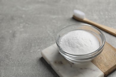 Photo of Bamboo toothbrush and bowl of baking soda on grey table, closeup. Space for text