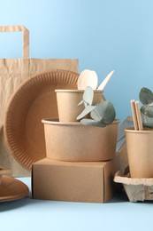 Eco friendly food packaging. Paper containers, tableware, bag and eucalyptus branches on white table against light blue background