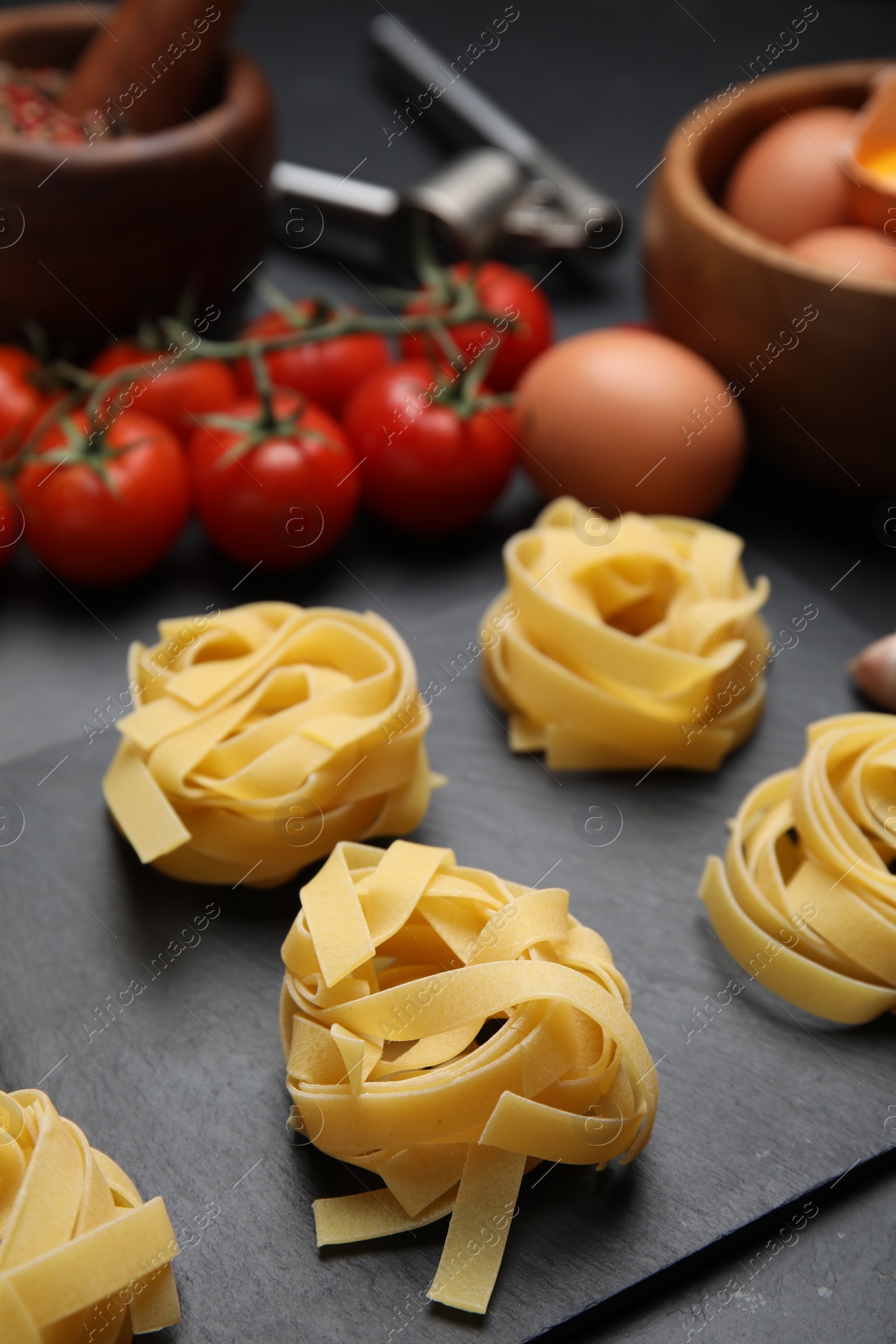 Photo of Uncooked tagliatelle and fresh ingredients on black table, closeup