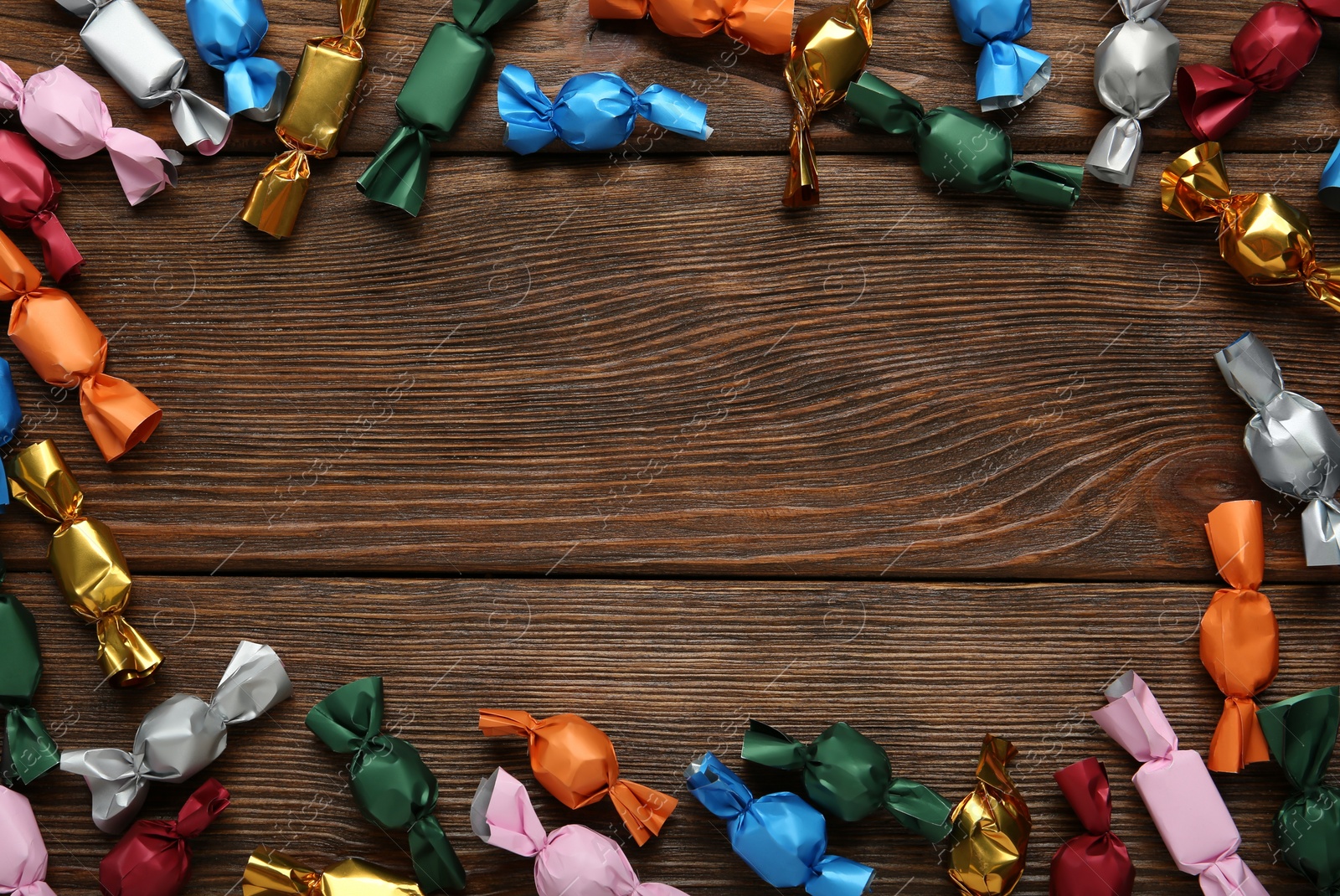 Photo of Frame of candies in colorful wrappers on wooden table, flat lay. Space for text