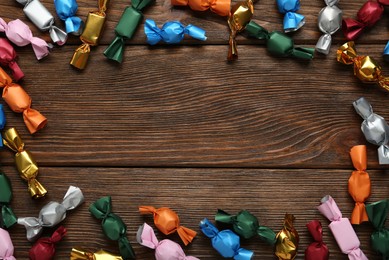 Frame of candies in colorful wrappers on wooden table, flat lay. Space for text