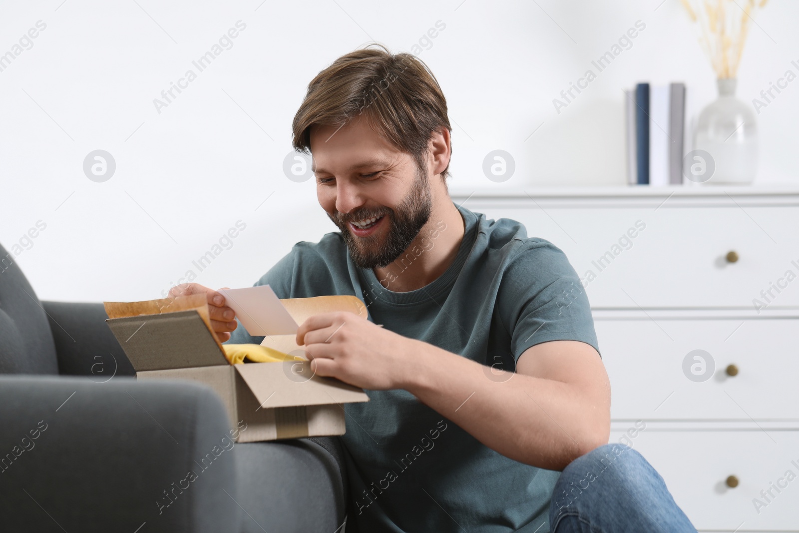 Photo of Happy man with greeting card near parcel at home. Internet shopping