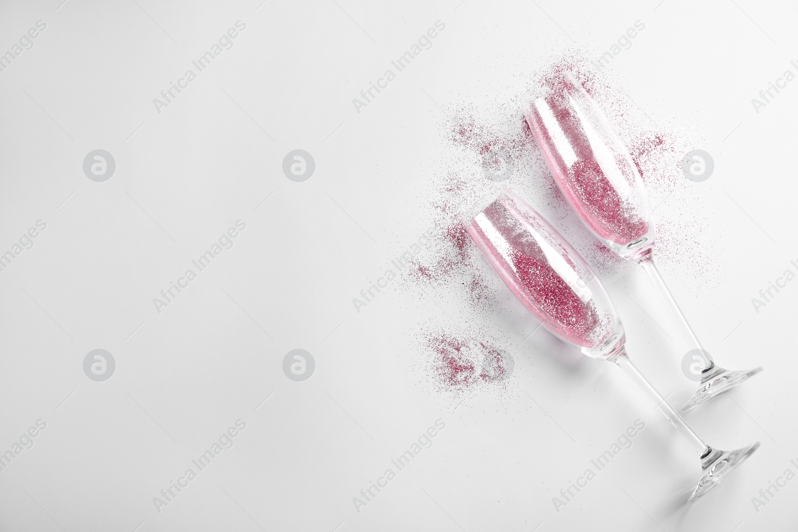 Photo of Champagne glasses with pink glitter and space for text on white background, top view. Hilarious celebration