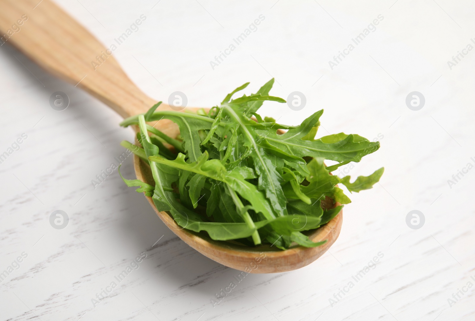 Photo of Fresh arugula in spoon on white wooden table, closeup