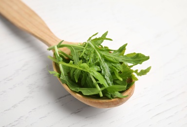 Fresh arugula in spoon on white wooden table, closeup