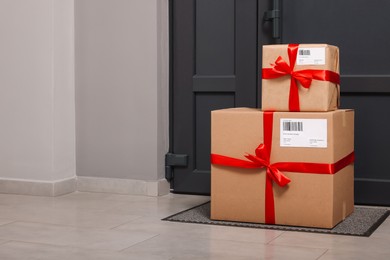 Photo of Christmas gift boxes on floor near door, space for text. Sending present by mail