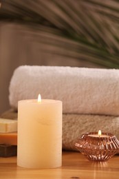 Spa composition with burning candles and towels on wooden table, closeup
