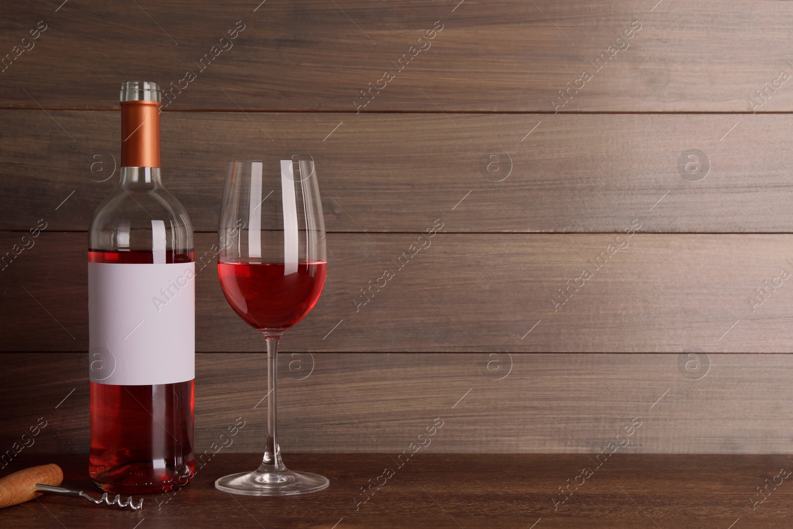 Photo of Corkscrew near bottle and glass of delicious rose wine on table against wooden background. Space for text
