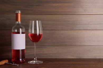 Corkscrew near bottle and glass of delicious rose wine on table against wooden background. Space for text