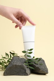 Woman with tube of cream, branches and stones on light yellow background, closeup