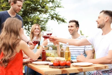 Photo of Young people with glasses of wine at table outdoors. Summer barbecue