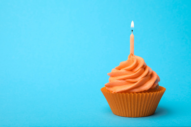 Delicious birthday cupcake with orange cream and burning candle on light blue background. Space for text