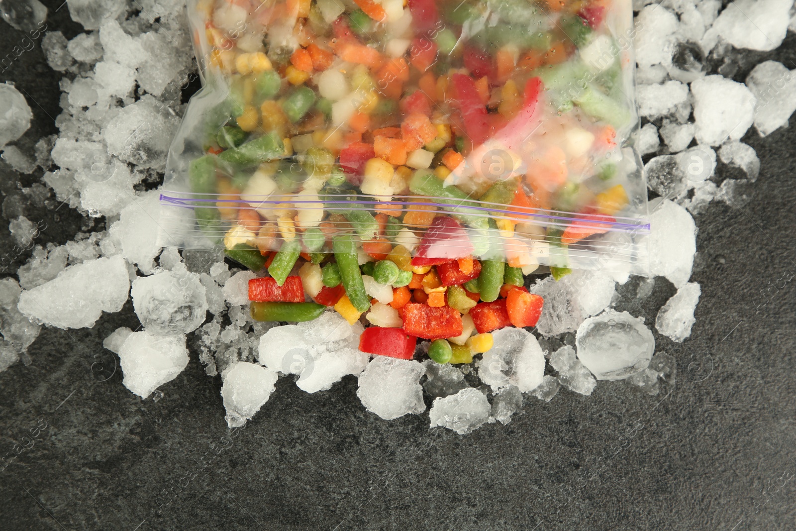 Photo of Zip bag with different frozen vegetables and ice on grey table, top view