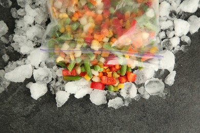 Photo of Zip bag with different frozen vegetables and ice on grey table, top view