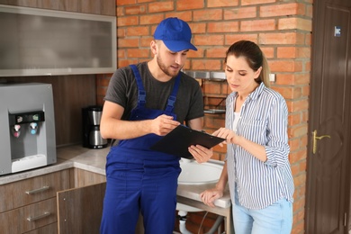 Professional plumber in uniform with client indoors