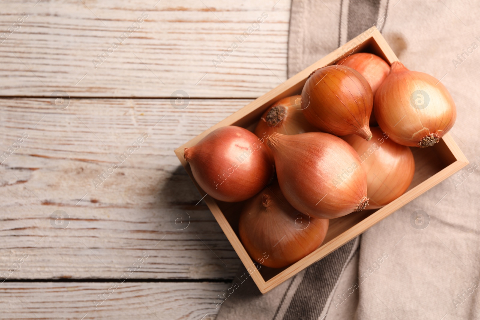 Photo of Crate with ripe onions on white wooden table, top view. Space for text