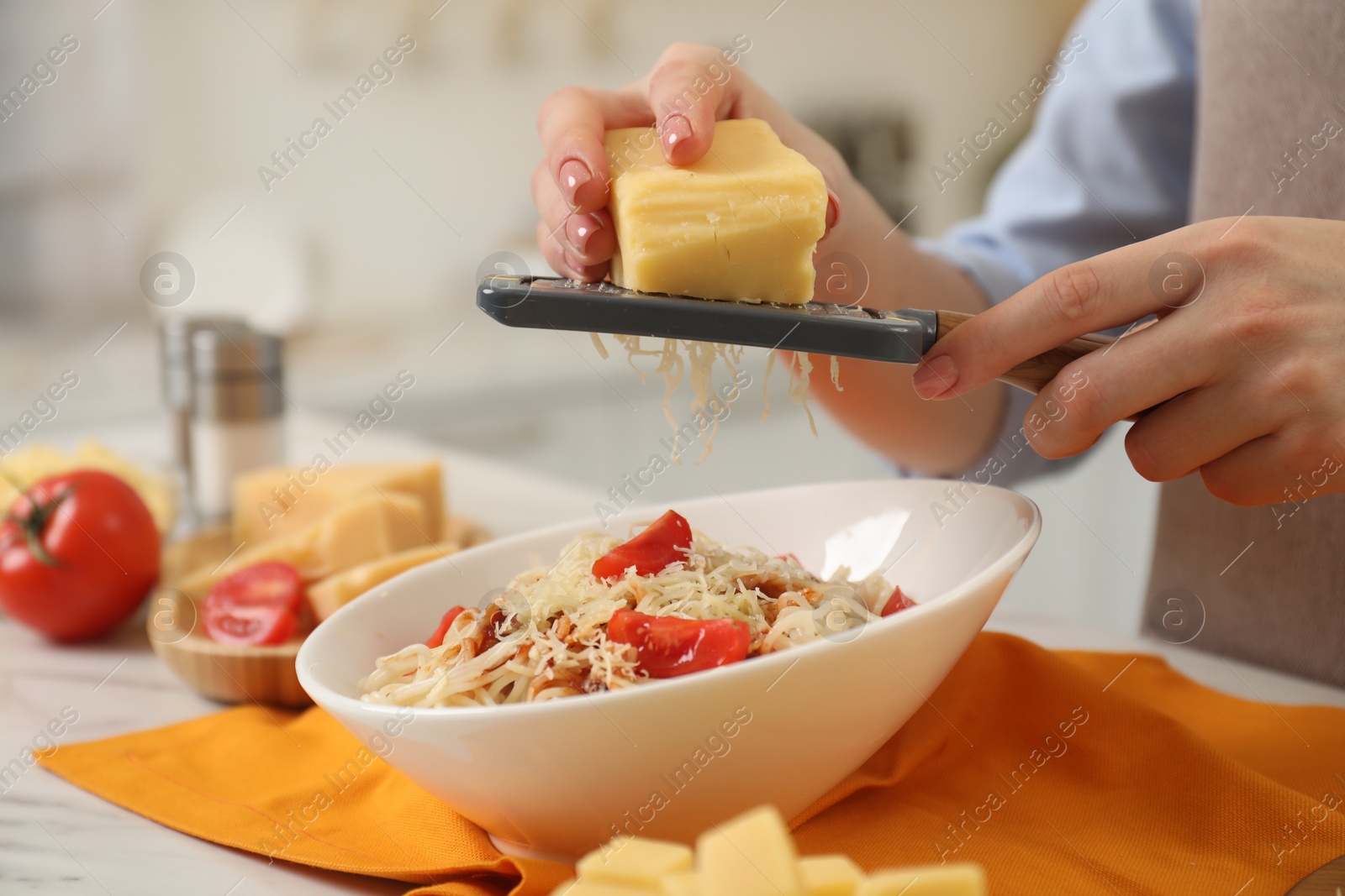 Photo of Woman grating cheese onto delicious pasta at white marble table in kitchen, closeup