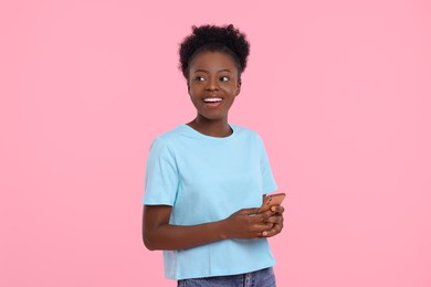 Happy young woman with smartphone on pink background
