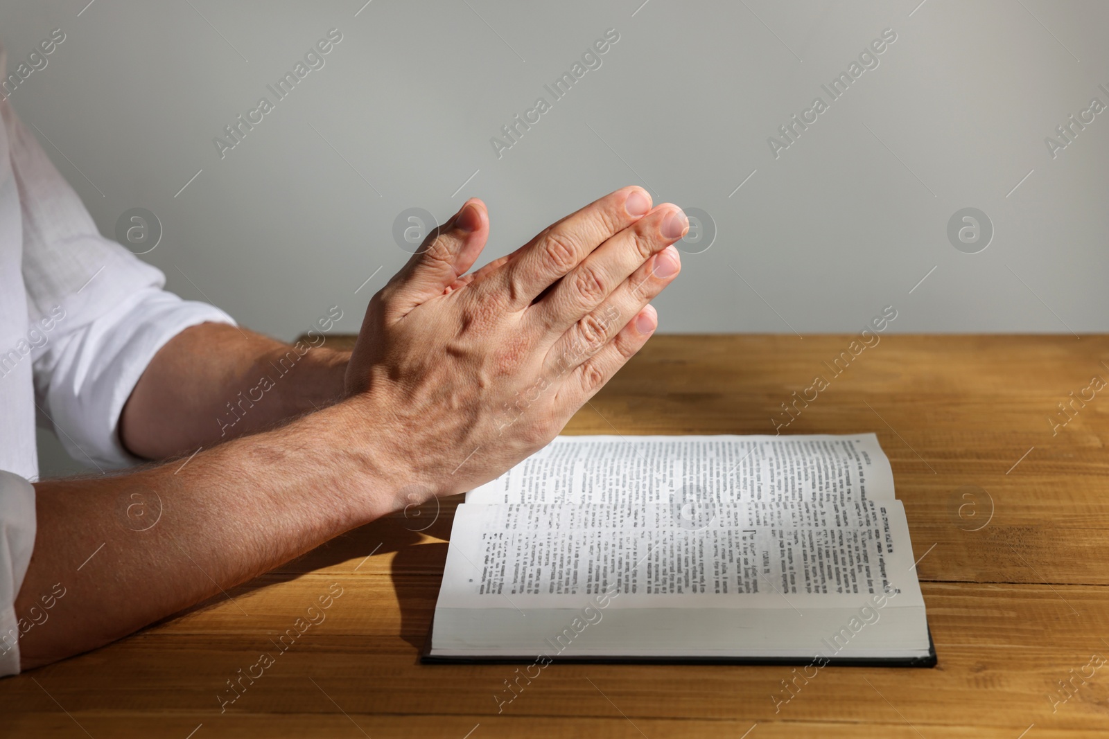 Photo of Man with Bible praying at wooden table, closeup