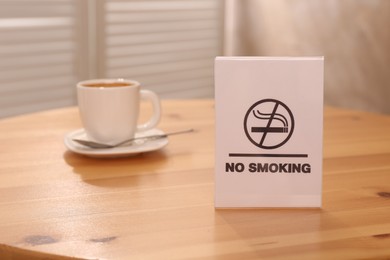 Photo of No Smoking sign and cup of drink on wooden table indoors, selective focus