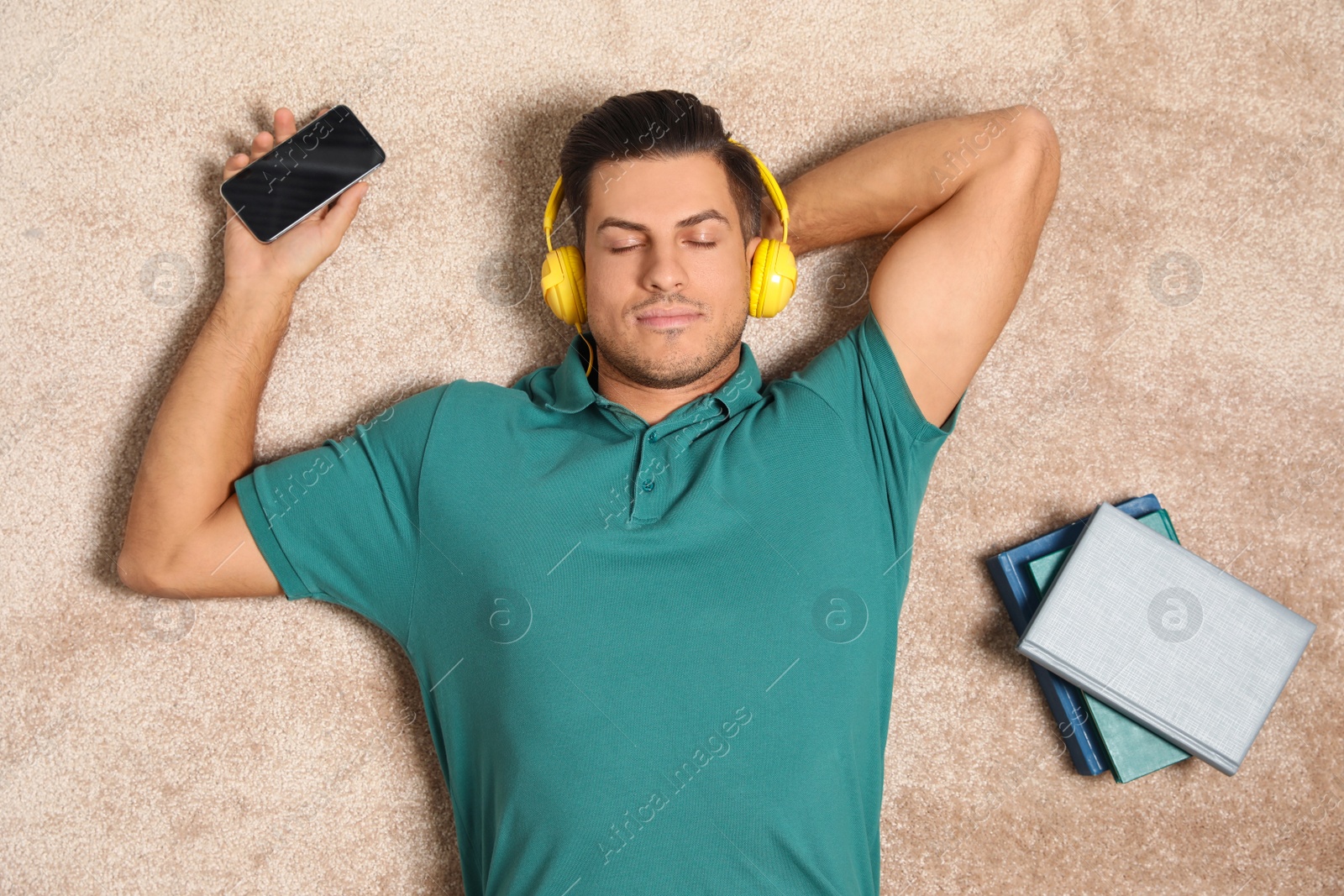 Photo of Man with smartphone listening to audiobook on floor, top view