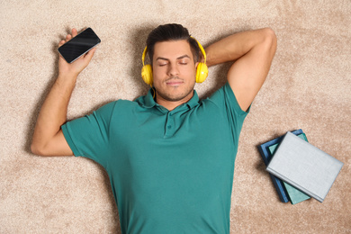 Man with smartphone listening to audiobook on floor, top view