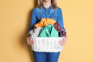 Photo of Woman holding laundry basket with dirty clothes on color background