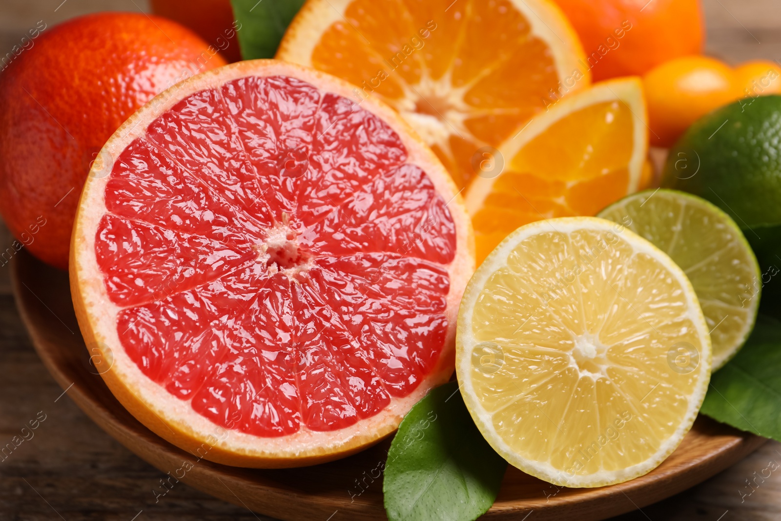 Photo of Fresh juicy citrus fruits with green leaves on wooden plate, closeup